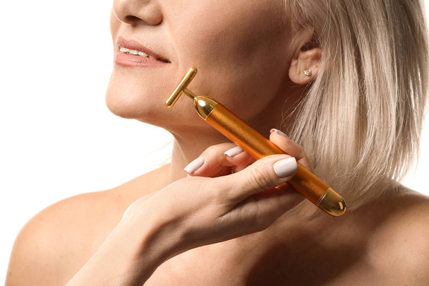 Mujer madura con herramienta de masaje facial sobre fondo blanco, primer plano
 - Foto, Imagen