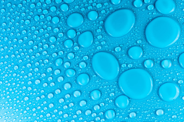 Droplets of water on a blue, matte background illuminated with a delicate light. - Zdjęcie, obraz