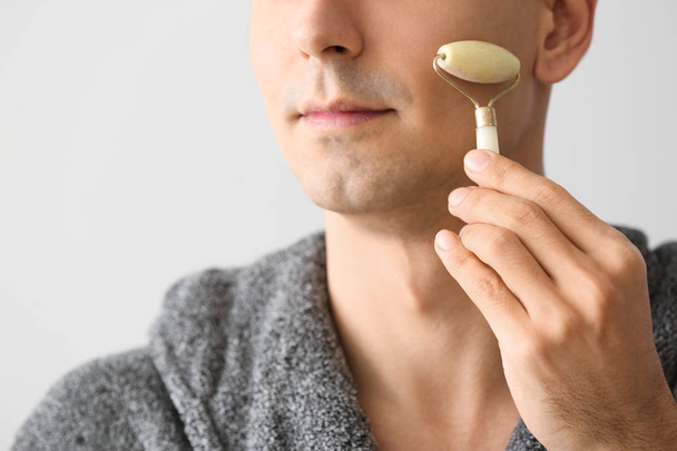 Hombre con herramienta de masaje facial sobre fondo claro
 - Foto, Imagen