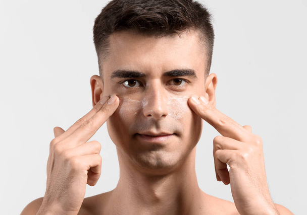 Man with applied face serum giving himself face massage on light background - Photo, Image