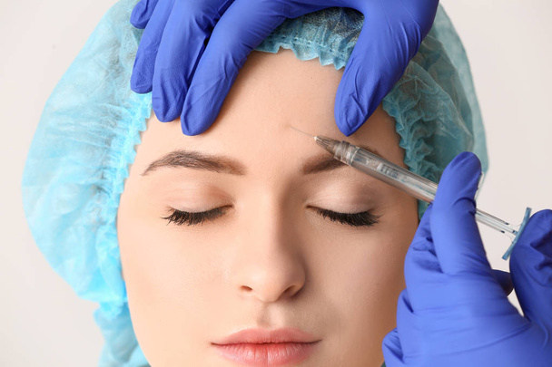 Jonge vrouw ontvangen injectie in gezicht op lichte achtergrond, close-up - Foto, afbeelding