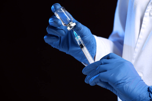 Cosmetologist holding syringe with filler and ampule on dark background, closeup - Photo, Image