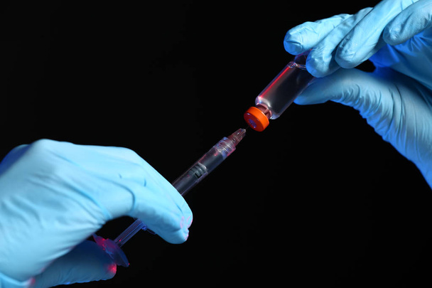 Cosmetologist segurando seringa com enchimento e ampola em fundo escuro, close-up
 - Foto, Imagem