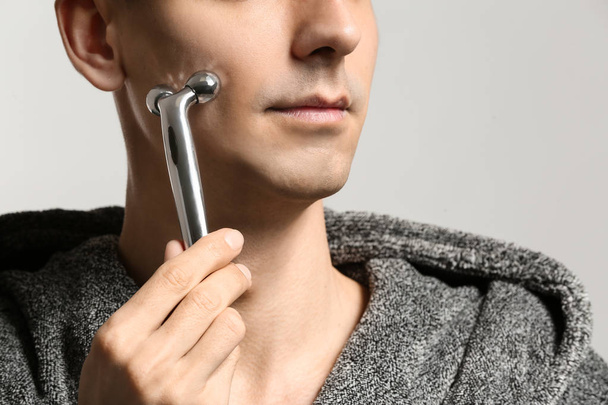 Man with facial massage tool on light background, closeup - Foto, immagini