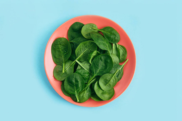 Green fresh vegetarian salad leaves on coral plate on blue background. Healthy and zero waste life concept. - Foto, imagen