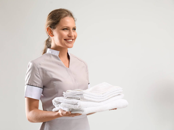 Portret van mooie vrouwelijke huishoudster met schone handdoeken op witte achtergrond - Foto, afbeelding