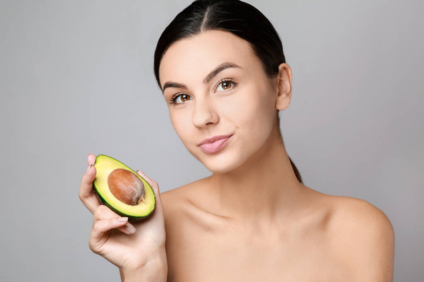 Portrait of beautiful woman with avocado on grey background - Photo, Image