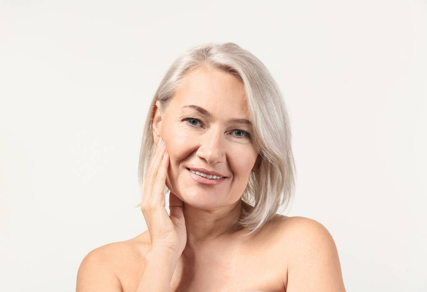 Mature woman giving herself face massage on light background - Photo, Image