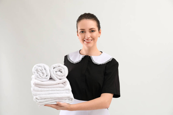 Retrato de hermosa ama de llaves con toallas limpias sobre fondo blanco
 - Foto, Imagen