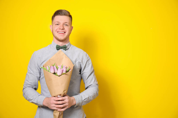 Young man with bouquet of flowers on color background. 8 March celebration - Foto, immagini