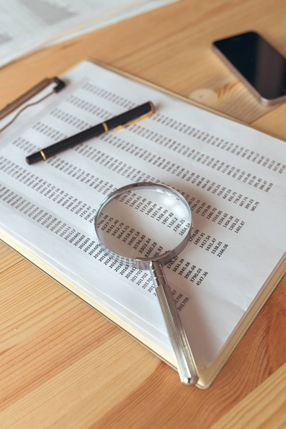 Business report analysis, magnifying glass over paper spreadshee - Fotó, kép