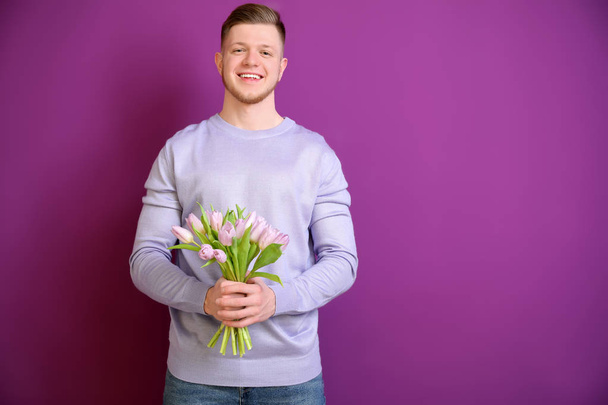 Giovane uomo con mazzo di fiori su sfondo a colori. 8 marzo celebrazione
 - Foto, immagini