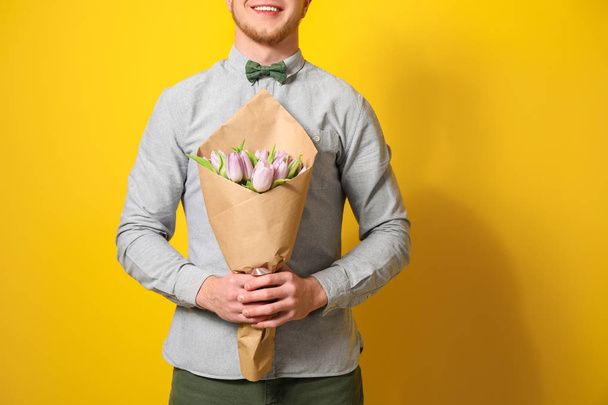 Młody człowiek z bukietem kwiatów na kolor tła. 8 marca święto - Zdjęcie, obraz