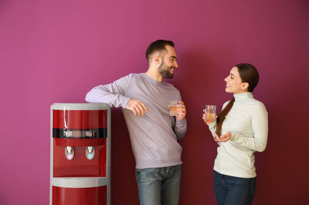 Мужчина и женщина пьют воду из холодильника на цветном фоне
 - Фото, изображение