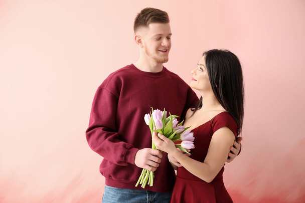 Young man greeting his wife with 8 March on color background - Foto, Imagen