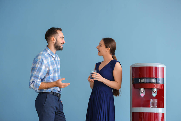 Homem e mulher bebendo água do refrigerador contra fundo de cor
 - Foto, Imagem
