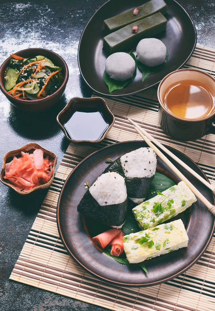 日本食の米のボールおにぎり、オムレツ、ジンジャー、酢の物ワカメきゅうりのミックス。豆と緑茶抹茶ゼリー羊羹、大福の餅の伝統的なデザート。アジアの朝食またはランチ - 写真・画像