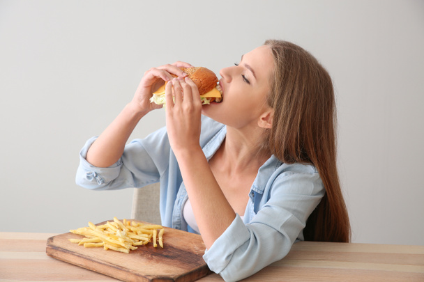 Fiatal nő evés ízletes burger és hasábburgonyával, asztal - Fotó, kép