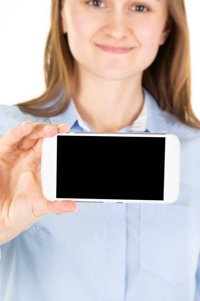 Imagen recortada de una joven hembra sosteniendo el teléfono celular con pantalla de copyspace negro posando en blanco pared del estudio en blanco
 - Foto, imagen