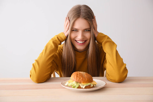 Young woman with tasty burger at table - Zdjęcie, obraz