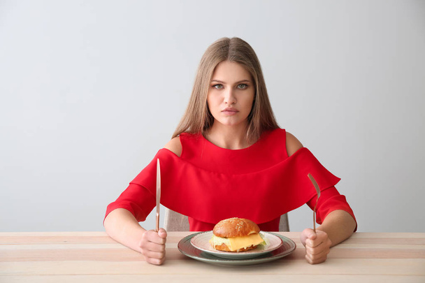 Jonge vrouw met lekkere Hamburger aan tafel - Foto, afbeelding