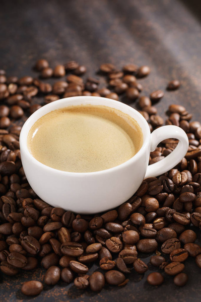 Coffee cup on roasted coffee beans. Dark background, sun rays. - Fotografie, Obrázek