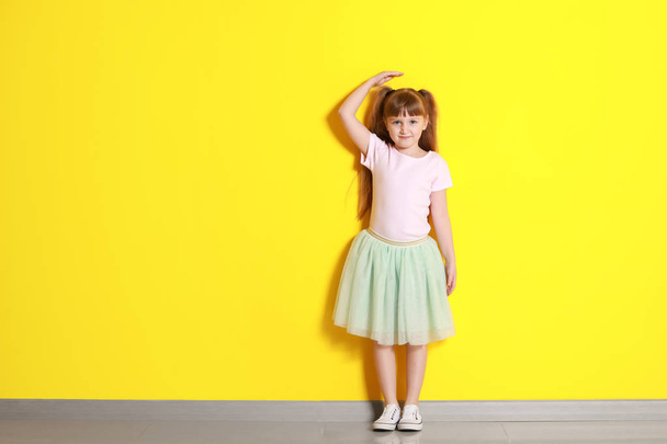 Cute little girl measuring height near color wall - Foto, afbeelding