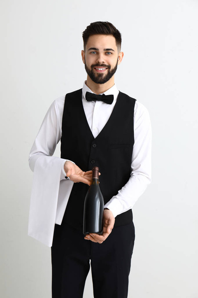 Handsome waiter with bottle of wine on light background - Фото, изображение