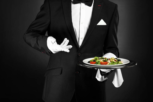Handsome waiter with fresh salad on dark background - Photo, Image