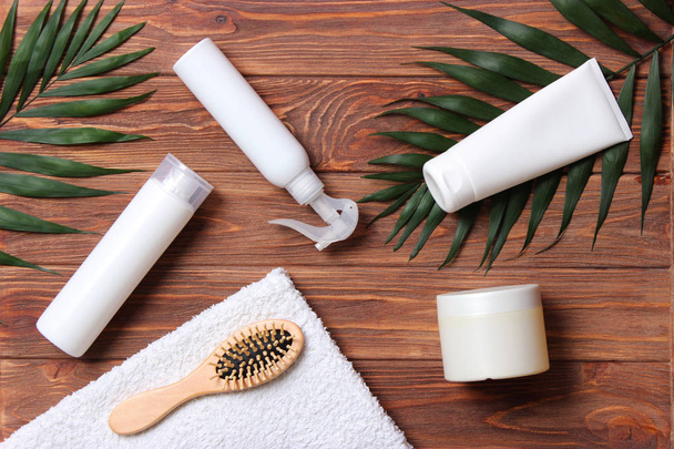 natuurlijke haarverzorgingsproducten, haarborstel, handdoek en bladeren op een houten achtergrond bovenaanzicht. Shampoo, masker, balsem. vlakke plaat - Foto, afbeelding
