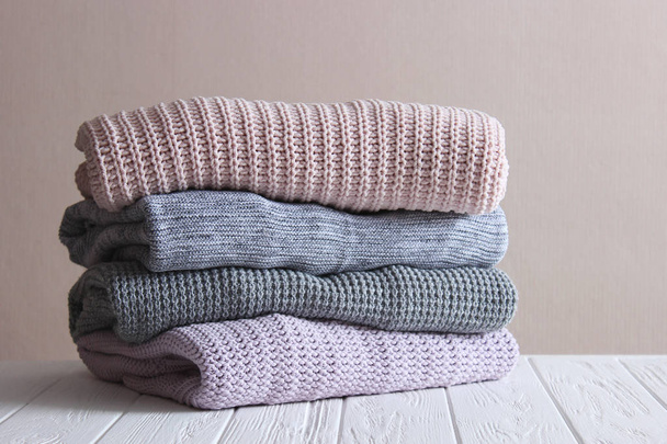 A pile of warm sweaters on a wooden table on a light background. Autumn and winter clothes. - Fotó, kép