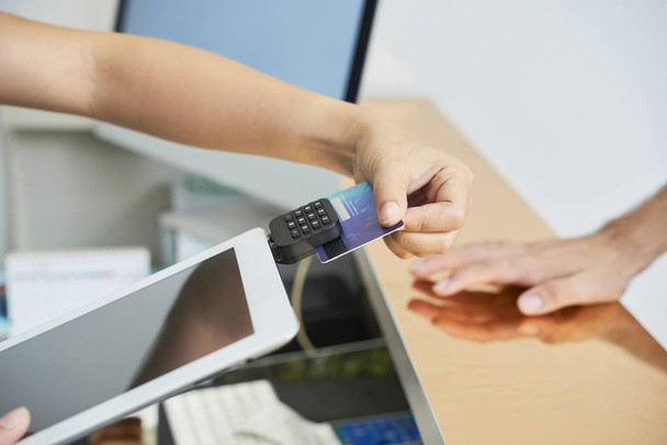 Cose-up de la réceptionniste féminine à l'aide d'une tablette numérique pour effectuer un paiement par carte de crédit avec le client debout près de la réception
  - Photo, image