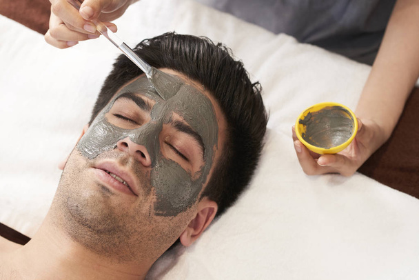 Mies saa kasvojen ravitseva savi naamio kosmetologi kylpylässä salonki
  - Valokuva, kuva
