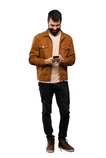 Bonito homem com barba enviando uma mensagem com o celular sobre fundo branco isolado
 - Foto, Imagem