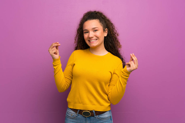 Teenager girl over purple wall making money gesture - Foto, imagen