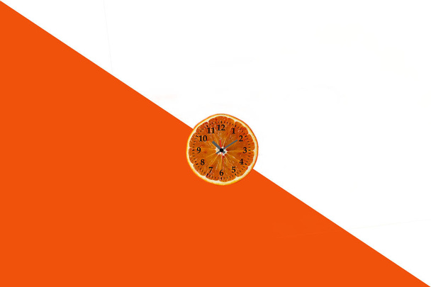 Flat lay of orange fruit slice with clock on white and orange pa - Valokuva, kuva