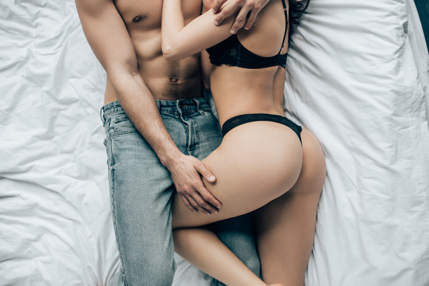 cropped view of shirtless man touching sexy woman in black underwear while lying on bed - Foto, afbeelding