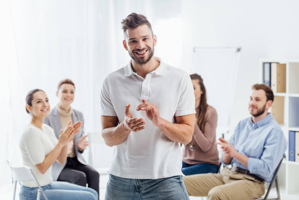 man looking at camera and applauding while people sitting during group therapy session - Foto, Imagen