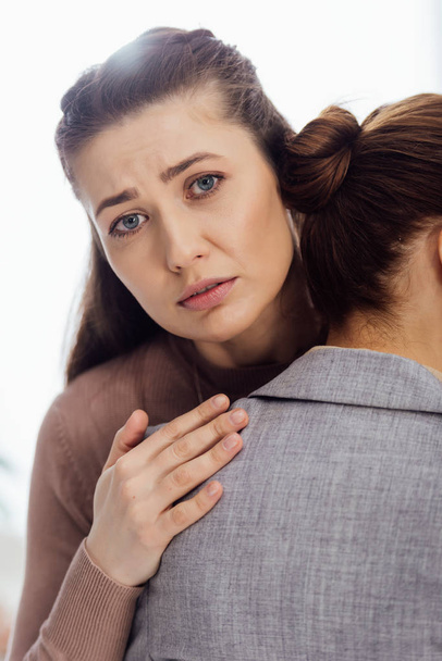 грустная женщина смотрит в камеру, обнимая другую женщину во время терапевтической встречи
 - Фото, изображение