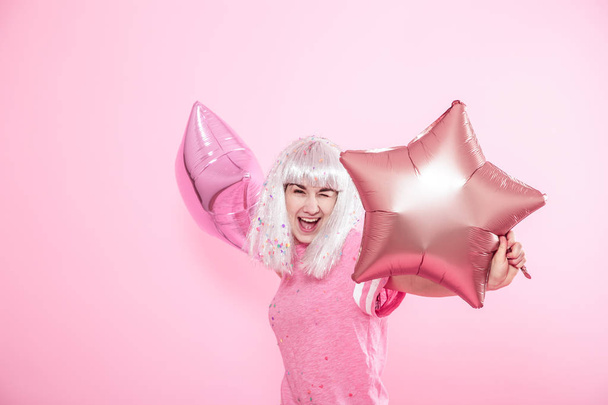 Αστείο κορίτσι με ασημένια μαλλιά δίνει ένα χαμόγελο και συγκίνηση σε ροζ φόντο. Νεαρή γυναίκα ή έφηβος κορίτσι με μπαλόνια και κομφετί - Φωτογραφία, εικόνα