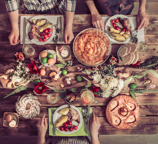 Amigos de vacaciones o familiares en la mesa de vacaciones con carne de conejo, verduras, pasteles, huevos, vista superior
. - Foto, imagen