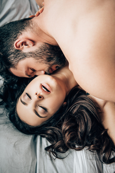 Ansicht des bärtigen Mannes, der attraktive sexy Frau auf dem Bett küsst  - Foto, Bild