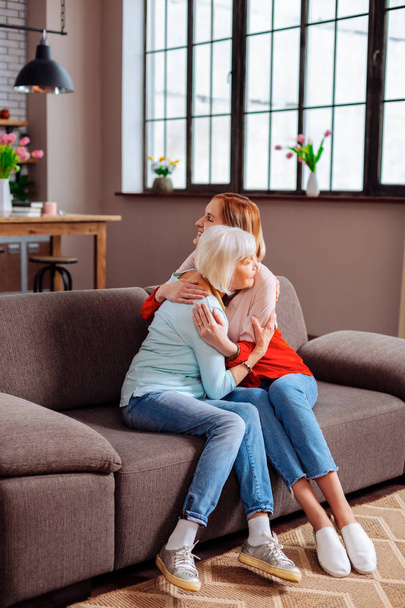 Elderly granny having a hug with attractive granddaughter on sofa - Photo, Image
