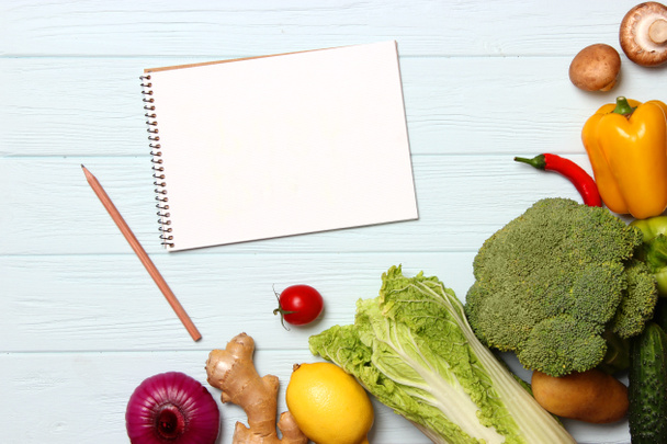 Farklı taze sebzeler ve tahta bir masanın üzerinde kağıt not defteri. Üst Manzara. Bir tarif, alışveriş listesi, satın alma ürünleri yaz. Yemek pişirmek. Düz Yatay  - Fotoğraf, Görsel