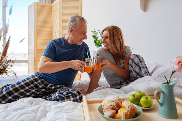 Couple clanging glasses with juice having breakfast in bed - Fotó, kép