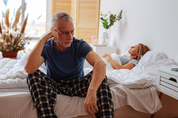 Grey-haired husband wearing pajamas sitting near sleeping wife - Foto, immagini