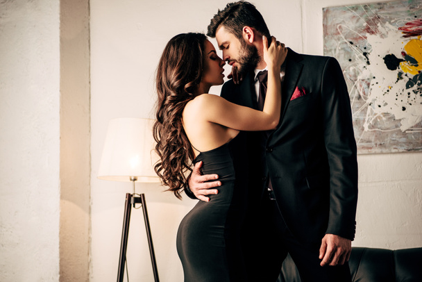 mulher atraente em vestido preto abraçando com homem apaixonado em terno
  - Foto, Imagem