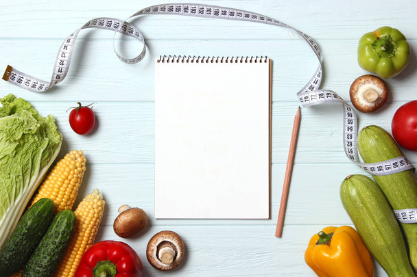 Friss zöldségek, mérőszalag és papír jegyzetfüzet az asztalon. Első látásra. Táplálkozási terv, megfelelő táplálkozás, fogyás, egészséges táplálkozás. lapos fektetés - Fotó, kép