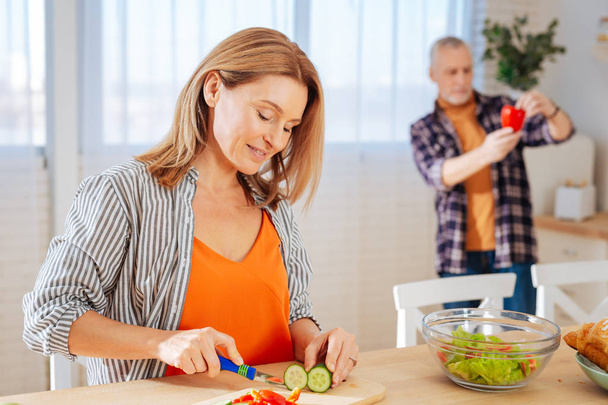 Appealing wife feeling joyful while cooking salad for husband - Photo, image