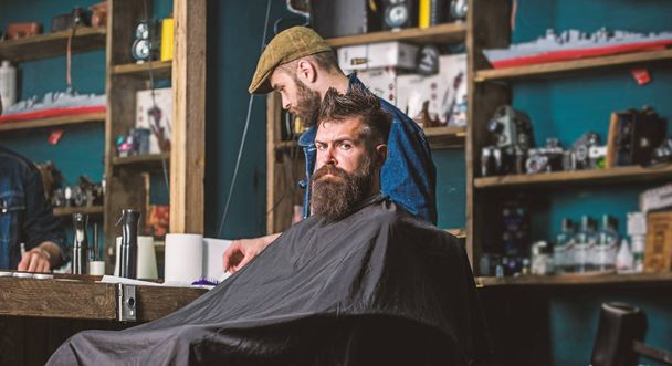Hipster client getting haircut. Client with beard ready for trimming or grooming. Haircut process concept. Man with beard covered with black cape waiting while barber changing clipper grade - Photo, image